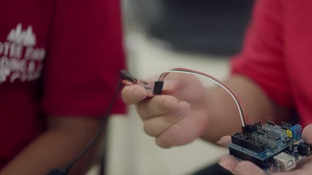 Close-up of hands connecting a sound sensor module to a microcontroller board during an Arduino STEM education project or electronics experiment.