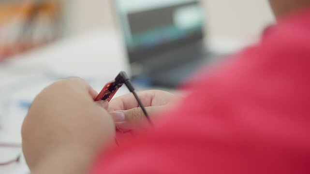 Close-up of student hands connecting wires to a red microcontroller board during a STEM electronics or Arduino programming activity.