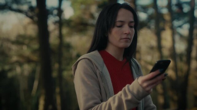  a young woman hiking in a forest as she video calls with her smartphone. With a bright smile and a backpack, she captures the moment amidst the natural scenery, reflecting the joy 