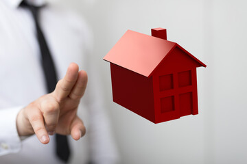 A businessman's hand pointing at a 3D red house, representing real estate, home ownership, and property investment. Focus on buying a house, mor © vegefox.com
