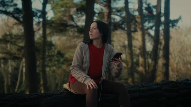  a young woman hiking in a forest as she video calls with her smartphone. With a bright smile and a backpack, she captures the moment amidst the natural scenery, reflecting the joy 