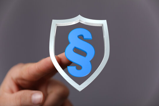 Conceptual image showcasing legal protection and the concept of law. A hand holding a shield with a paragraph symbol. Ideal for legal or complia