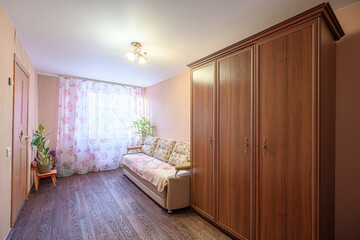 Cozy living room with wooden wardrobe, beige sofa with floral cushions, floral curtains, potted...