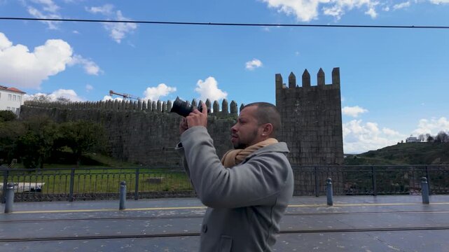 Man taking photos near medieval castle walls
Photographer capturing images near historic fortress architecture under blue sky.