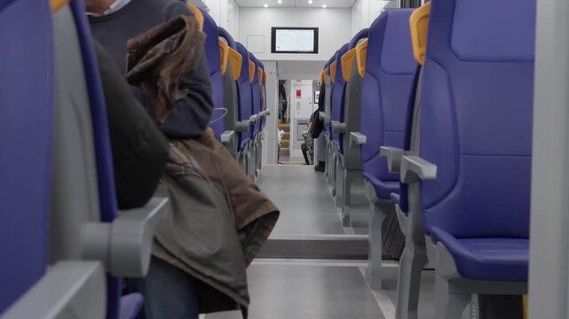Inside the lower deck of a moving double decker passenger train during travel. Blue seats and aisle swaying slightly in motion. Railway transit with digital screen and commuters on trip.