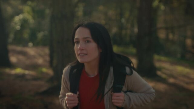  a young woman hiking in a forest, showcasing her determination and connection to nature, looking up as she walks along a trail surrounded by trees and dappled sunlight.