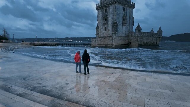 Couple standing near Belem Tower on cloudy day
People near the historic Bel&eacute;m Tower by the river under dramatic cloudy weather in Lisbon.