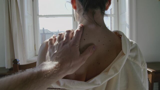 Man's hand touching woman's back with moles near window. Represents skin care, dermatology check or intimacy. Perfect for medical ads, health videos or romantic scenes.