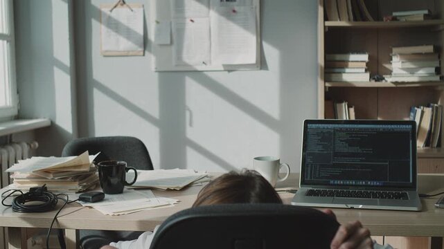 A tired young man slides down his chair and disappears under the desk. This scene depicts burnout, frustration, or procrastination, suitable for work-related content.