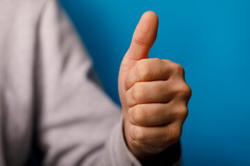 Close-up of a hand with a thumbs up gesture against a blue backdrop, symbolizing positive emotions like approv