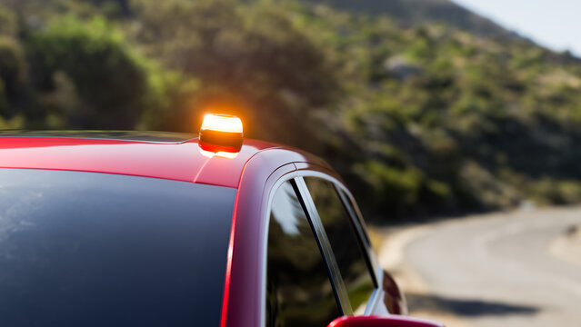 Close-up of a red car with a V16 beacon flashing on its roof, stopped on a mountain road during the day. Road safety concept and new regulations for V16 emergency signaling devices in realistic 3D