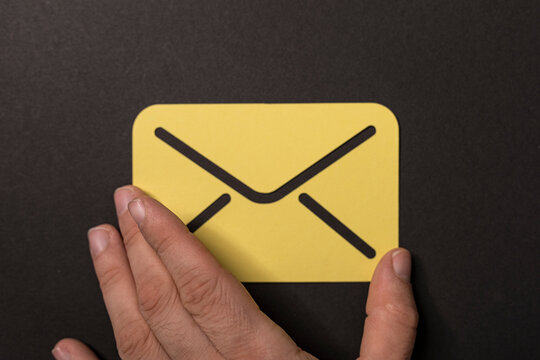 Close up shot of a hand positioning a yellow email icon on a dark surface, symbolizing communication and messagi