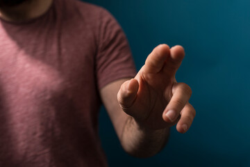 Close up shot of a man pointing with his finger. The hand gesture is highlighted against a blue background, perf