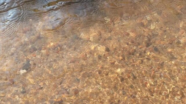 Peaceful clear shallow stream water flowing over brown stone pebble rock texture background showing natural tranquility of sand creek bed bottom with calm relaxing wave movement pure nature fresh
