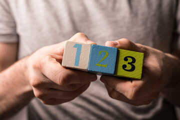 Close-up of a man's hands holding wooden blocks arranged sequentially, with the numbers one, two, and three disp