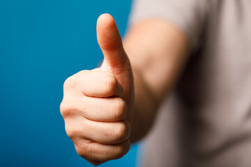 Hand gesture showing thumbs up with a blue background. Positive and approval concept. Ideal for success and ag