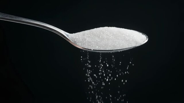 High-quality close-up of sugar granules falling from a spoon on a dark background