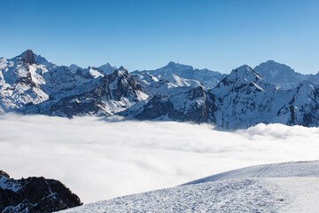 Majestic view of snow-covered mountains with clouds at the base under a clear blue sky. Perfect for