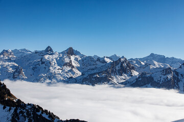Dramatic mountain peaks covered in snow rise above a sea of clouds under a clear blue sky. Serene wi