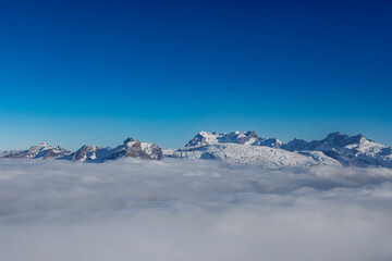 Stunning landscape of snow-capped mountains peaking above a sea of clouds under a bright blue sky. P