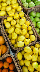 Abundance of fresh lemons, tangerines and green pears in wicker baskets at a local farmer market