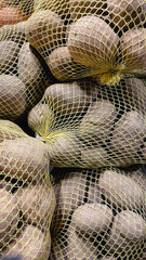 Potatoes packed in yellow mesh bags for sale. Raw organic vegetable harvest background in wholesale