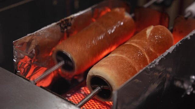 Traditional christmas chimney cake, kurtos kalacs, trdelnik, and polish kołacz slowly rotating and roasting over an open charcoal fire at a festive holiday market