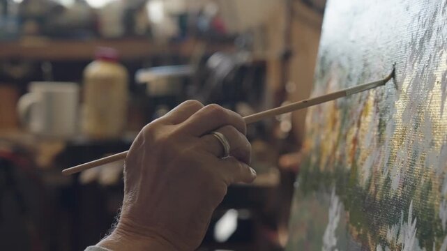 Senior artist on a wheelchair paints an oil painting on canvas in a studio