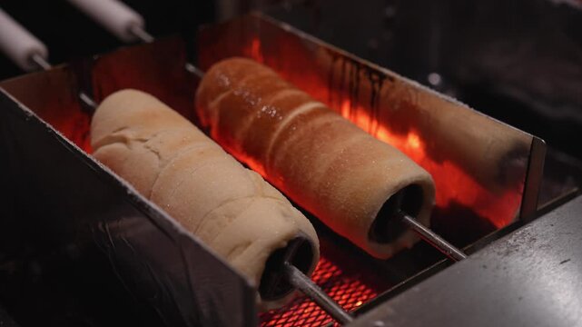 Traditional christmas chimney cake, kurtos kalacs, trdelnik, and polish kołacz slowly rotating and roasting over an open charcoal fire at a festive holiday market