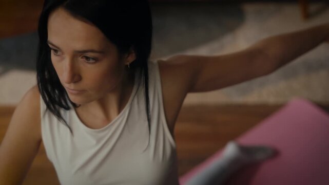 woman practising yoga in a cosy living room setting. She is in a lunging pose on a yoga mat, with a tablet in front of her displaying a workout or meditation session. 