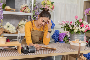 Florist shopkeeper startup small business owner feeling worried about business growth, reviewing expenses and orders at flower shop counter, facing financial concern, woman shop entrepreneur headache