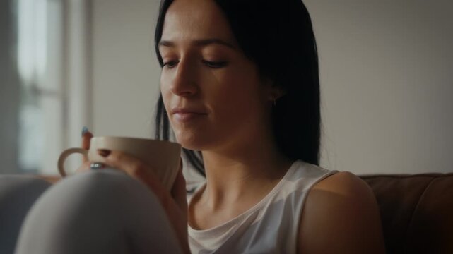 woman sipping tea or coffee in a cosy living room setting. Warm lighting.