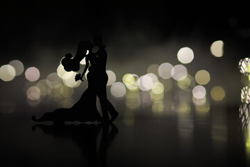 Black silhouettes of pair dancers performing. Man and woman are dancing on gray background with white backlight. Choreography. New Year's ball