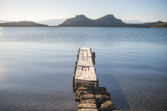 Rustic Weathered Wooden Pier Extending into the Still Blue Waters of Lake Vouliagmeni, Greece