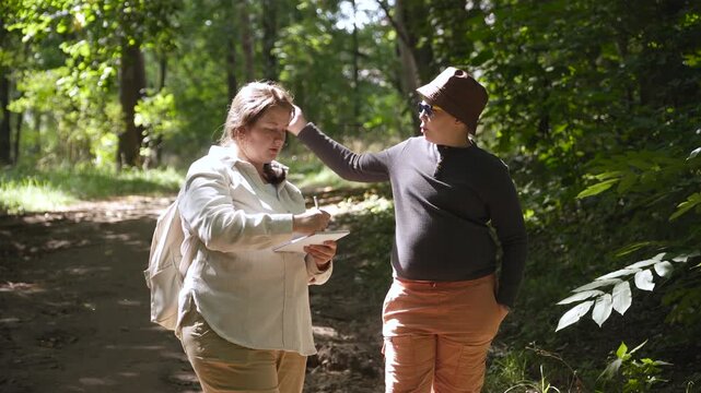 Mother and son swat away pesky mosquitoes and midges during walk in park. Risk of summer insect bites. Woman sketches nature during family nature walk.