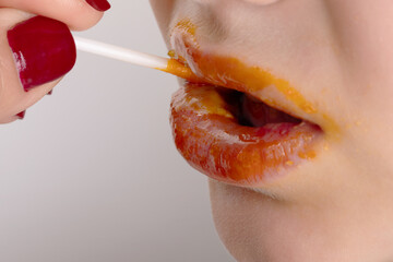 Close-up of woman's lips with orange gloss being applied, highlighting vivid color and beauty detail. Focus on glossy texture and modern makeup style.