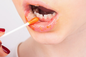 Close-up of a woman using a cotton swab to apply orange lip balm, showing detailed texture of lips and skin. Fresh, clean, and suitable for beauty or skincare concepts.