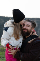 Smiling bearded father embraces his daughter in warm winter clothing outdoors, capturing a moment of love, family, and togetherness.