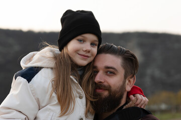 Smiling father embraces his daughter in warm outdoor clothing, showcasing family love and togetherness in a natural setting.