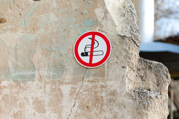No smoking sign on a weathered stone wall, emphasizing health and safety regulations in outdoor environments.