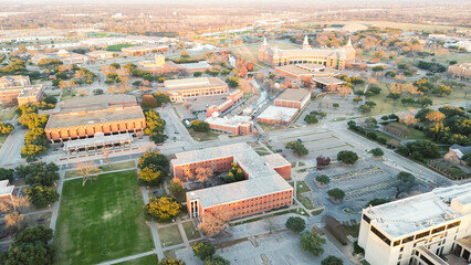 Flat-roofed structures with canal winds through college campus, surrounded by surface parking lots, fall foliage trees, pathway, architectural focal point within academic layout, Waco, Texas