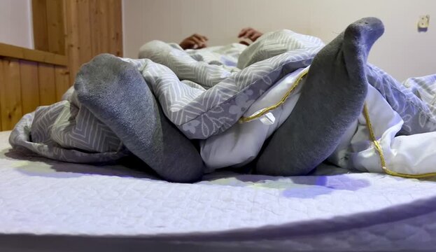 Feet wearing grey socks sticking out from under the blanket while sleeping in bed