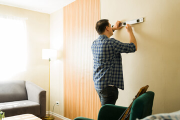 Man holding a level tool and marking a wall, performing home renovation and decoration as a do-it-yourself project