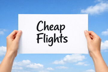 Hands holding a white paper sign that reads cheap flights against bright blue sky.
