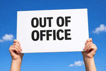 Two raised hands hold a white paper sign with Out of Office text with clear blue sky.