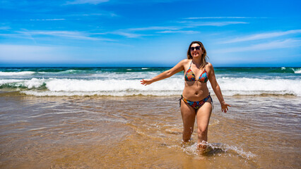 Fototapeta premium Beautiful middle-aged woman walking in ocean on sunny summer day. Front view 