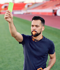 Portrait of a  soccer referee blowing a whistle and showing a yellow red card on stadium soccer...