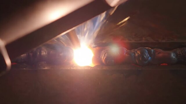 Close Up of Welding Process with Bright Sparks and Molten Metal in Dark Workshop Setting
