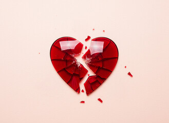 Closeup of broken heart shape in red glass isolated on pink background, symbolising heartbreak, love, grief, centre aligned