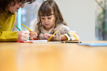 Child focused on drawing while mother assists her